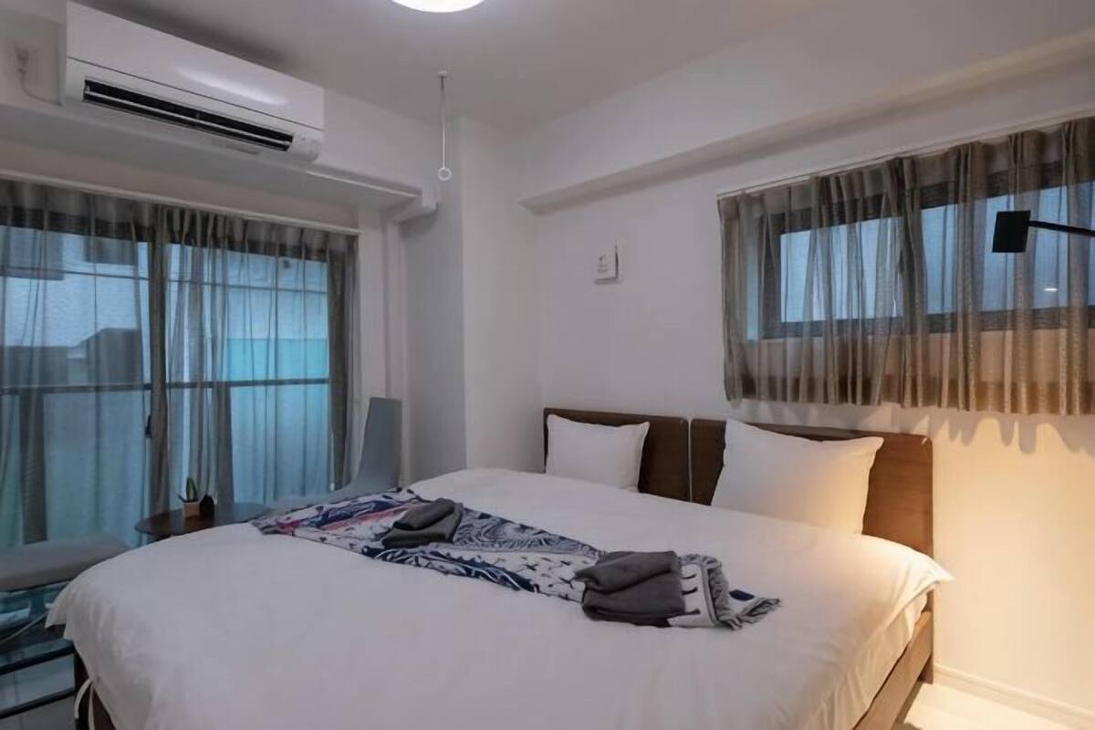 A hotel room with a bed, air conditioning unit, and a window with curtains.