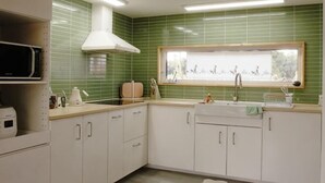 A kitchen with white cabinets, a microwave, a stove, and a window with a view of the outdoors. - Thechaeum (Seogwipo)