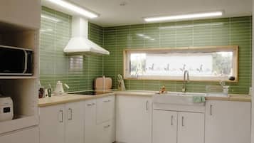Una cocina con gabinetes blancos, microondas, estufa y ventana con vista al exterior.