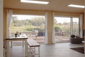 A spacious room with a large sliding glass door leading to a balcony, a wooden dining table, and a gray sofa. - Thechaeum (Seogwipo)