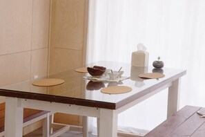 A dining table with a glass top, white frame, and placemats. - Thechaeum (Seogwipo)