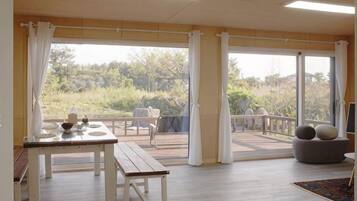 A spacious room with a large sliding glass door leading to an outdoor area, a dining table with chairs, and a seating area with cushions.