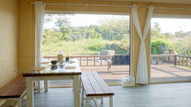A room with a wooden bench, a table with a bowl and a cup, and a view of a balcony with outdoor furniture. - Thechaeum (Seogwipo)