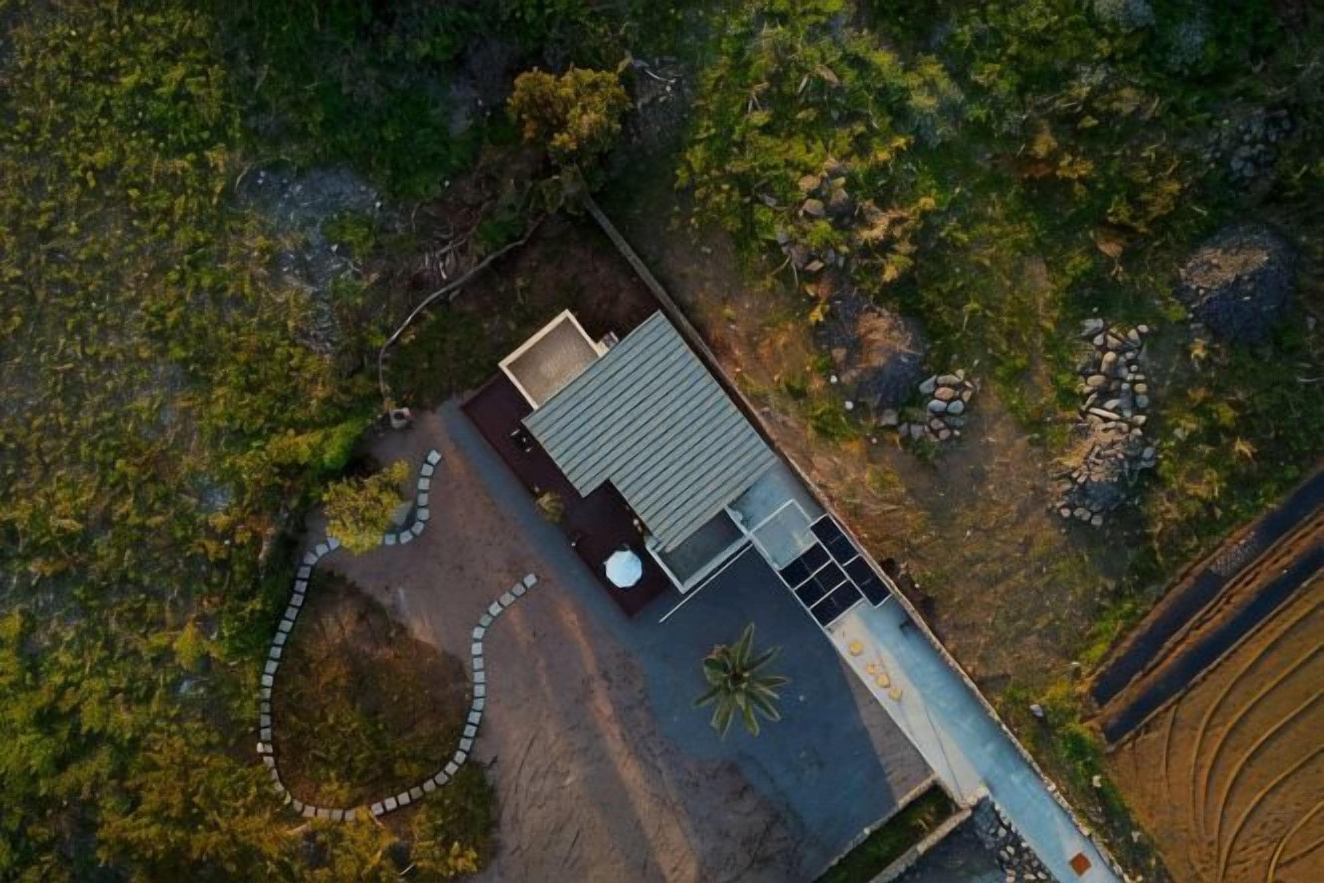 An aerial view of a house with a flat roof, a driveway, and a garden area.