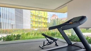 A treadmill in a room with a large window, a bench, and a view of a building with yellow and green facades.