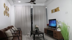 A living room with a brown sofa, a coffee table with a vase, a TV on a wooden stand, and a ceiling fan.