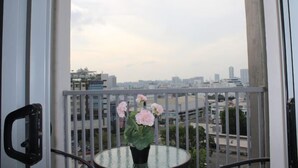 A balcony with a glass table and a vase of flowers, overlooking a cityscape.