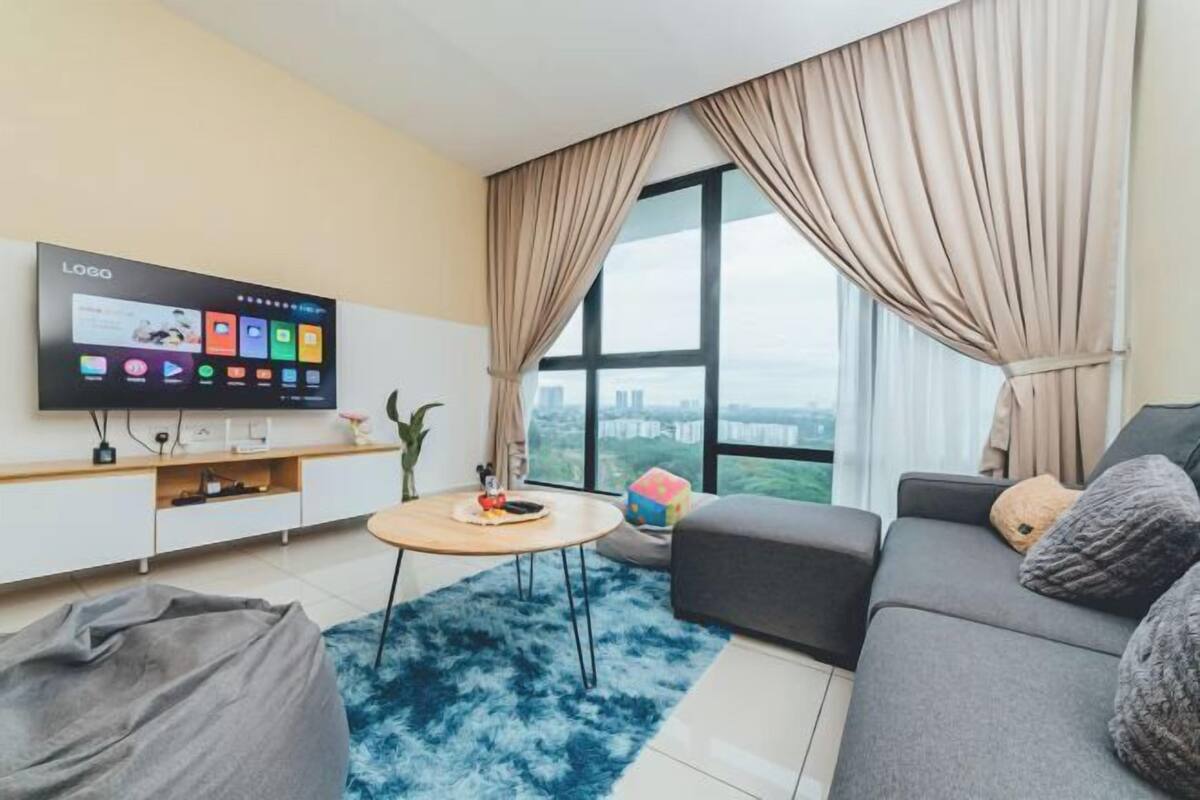 A modern living room with a large TV, a sofa, a coffee table, and a view of the city through large windows.