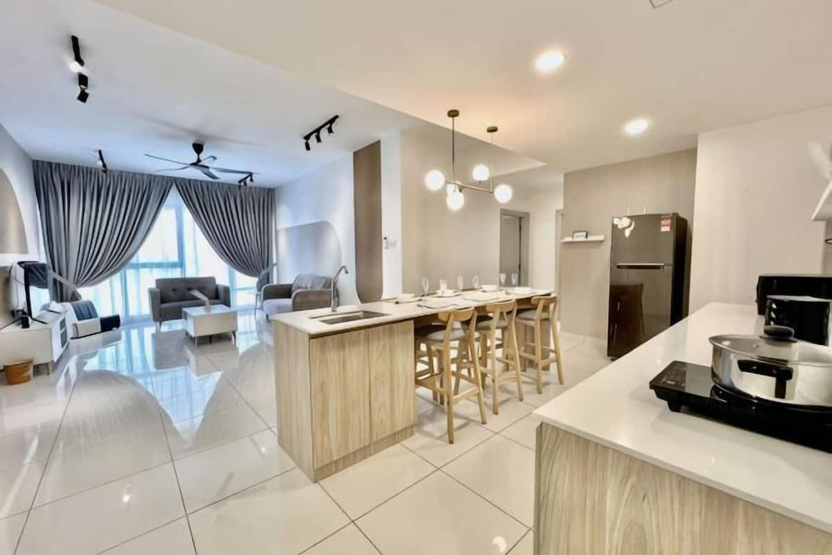A modern kitchen with a central island, bar stools, a refrigerator, and a dining area.