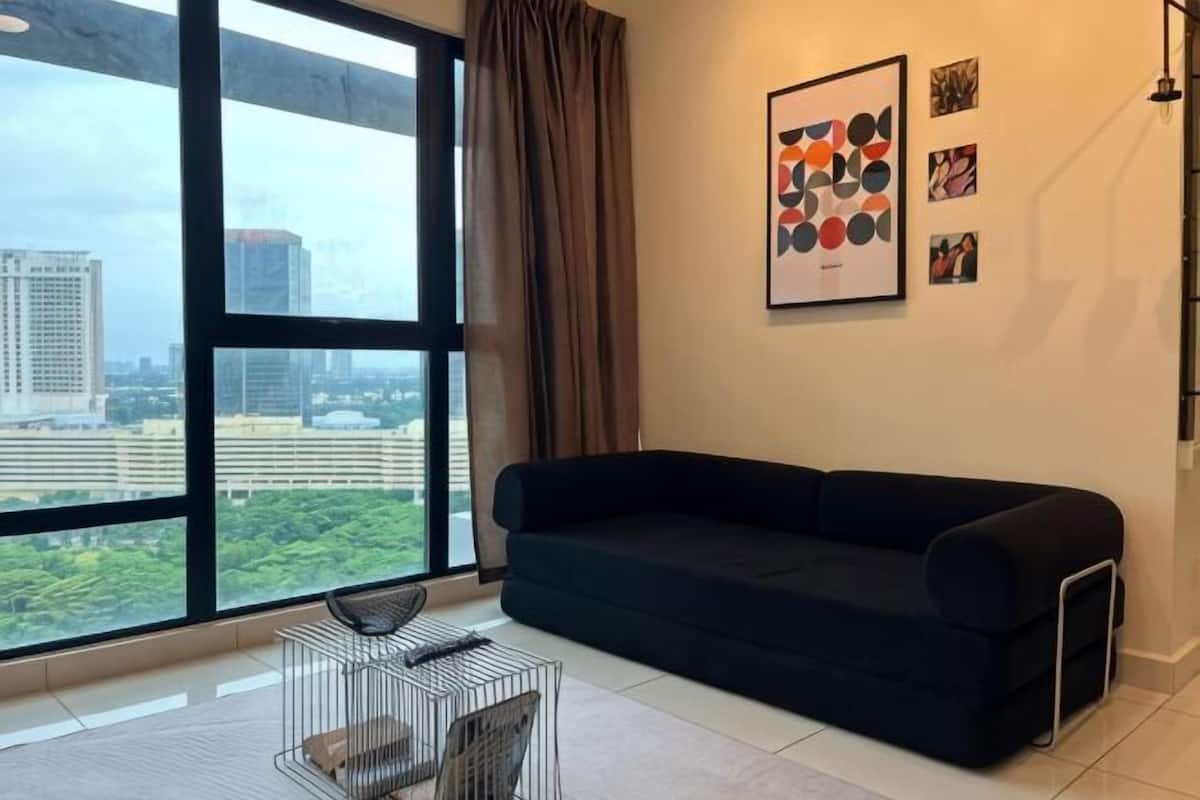 A modern living room with a black sofa, a metal coffee table, and a large window offering a city view.