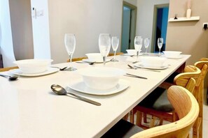 Une table à manger dressée avec de l’assiette, des bols et des couverts blancs, entourée de chaises en osier.