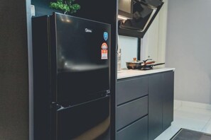 Un réfrigérateur noir orné d’un autocollant, un plan de travail de cuisine avec une casserole, et des meubles de rangement sombres.