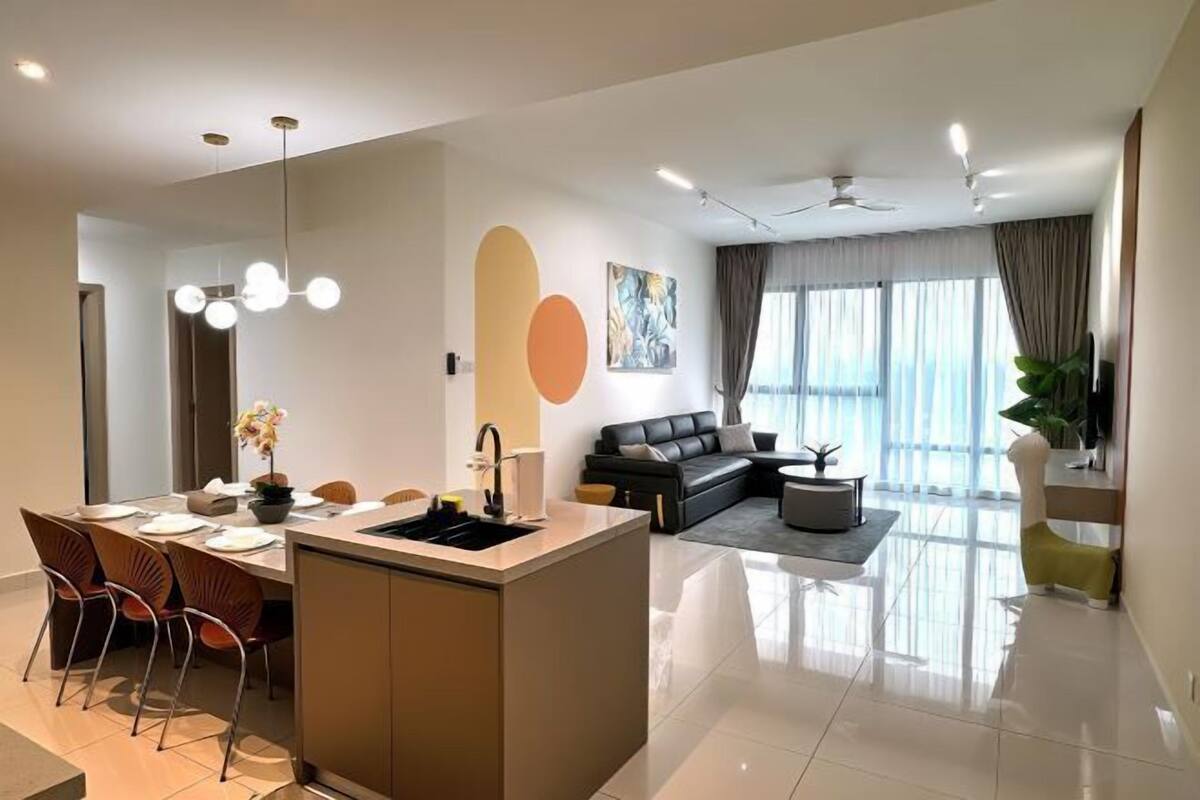 A modern living room with a sofa, a dining area with chairs, a kitchen island, and a large window.