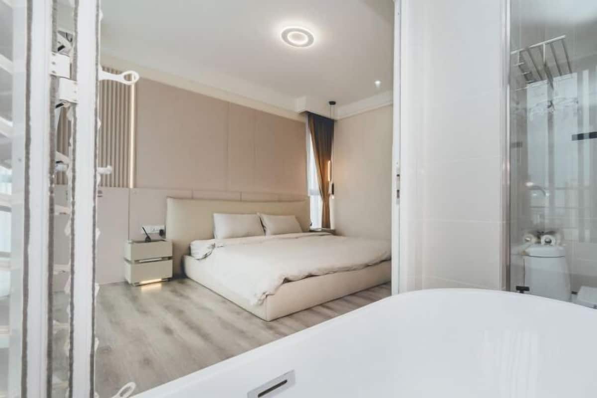 A modern bedroom with a large bed, bedside tables, and a bathroom with a shower.
