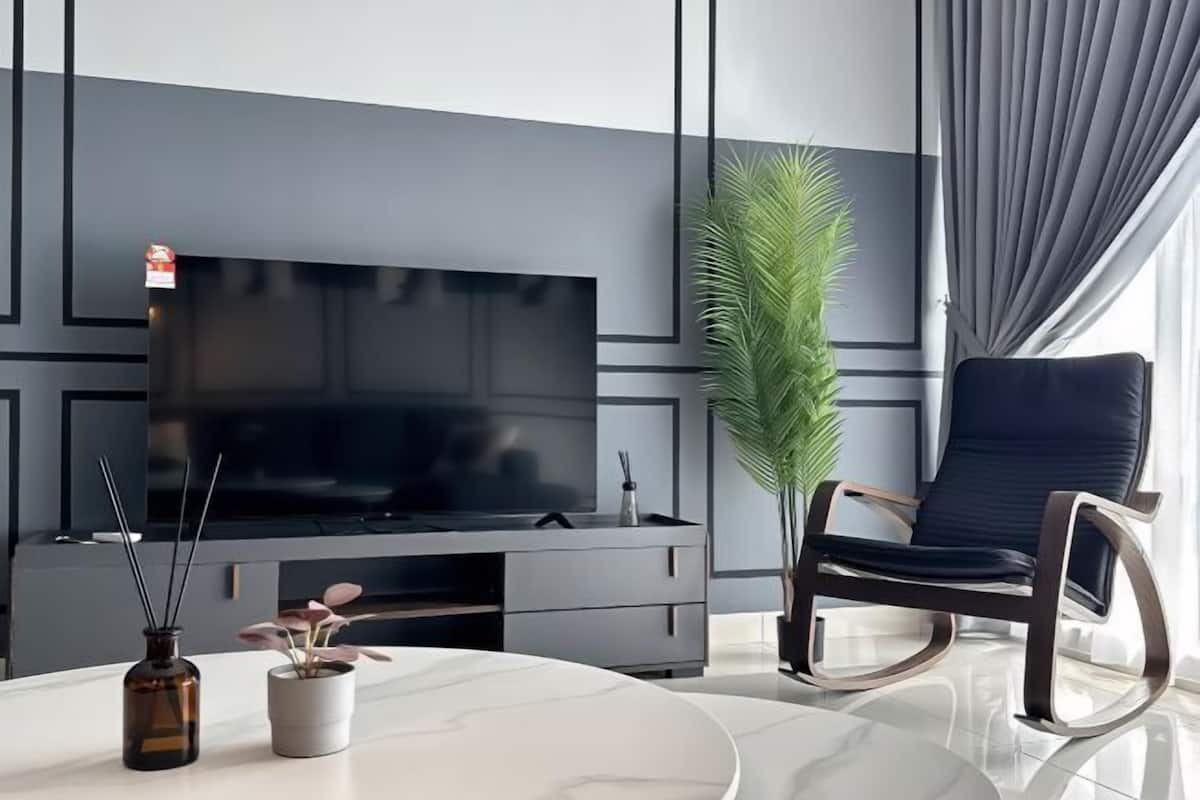 A modern living room with a flat-screen TV on a dark console, a round marble table with a vase and a potted plant, and a black leather chair.