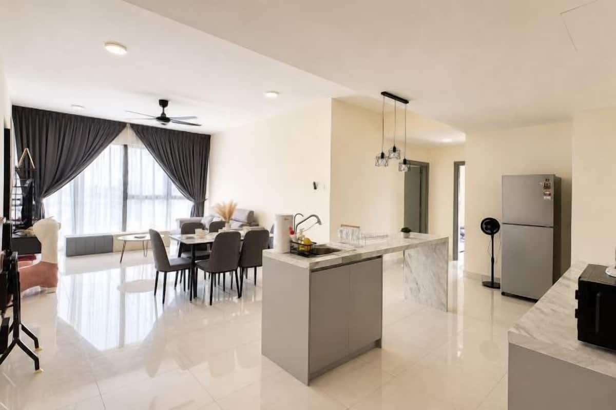 A modern kitchen with a central island, dining area with chairs, and a refrigerator.