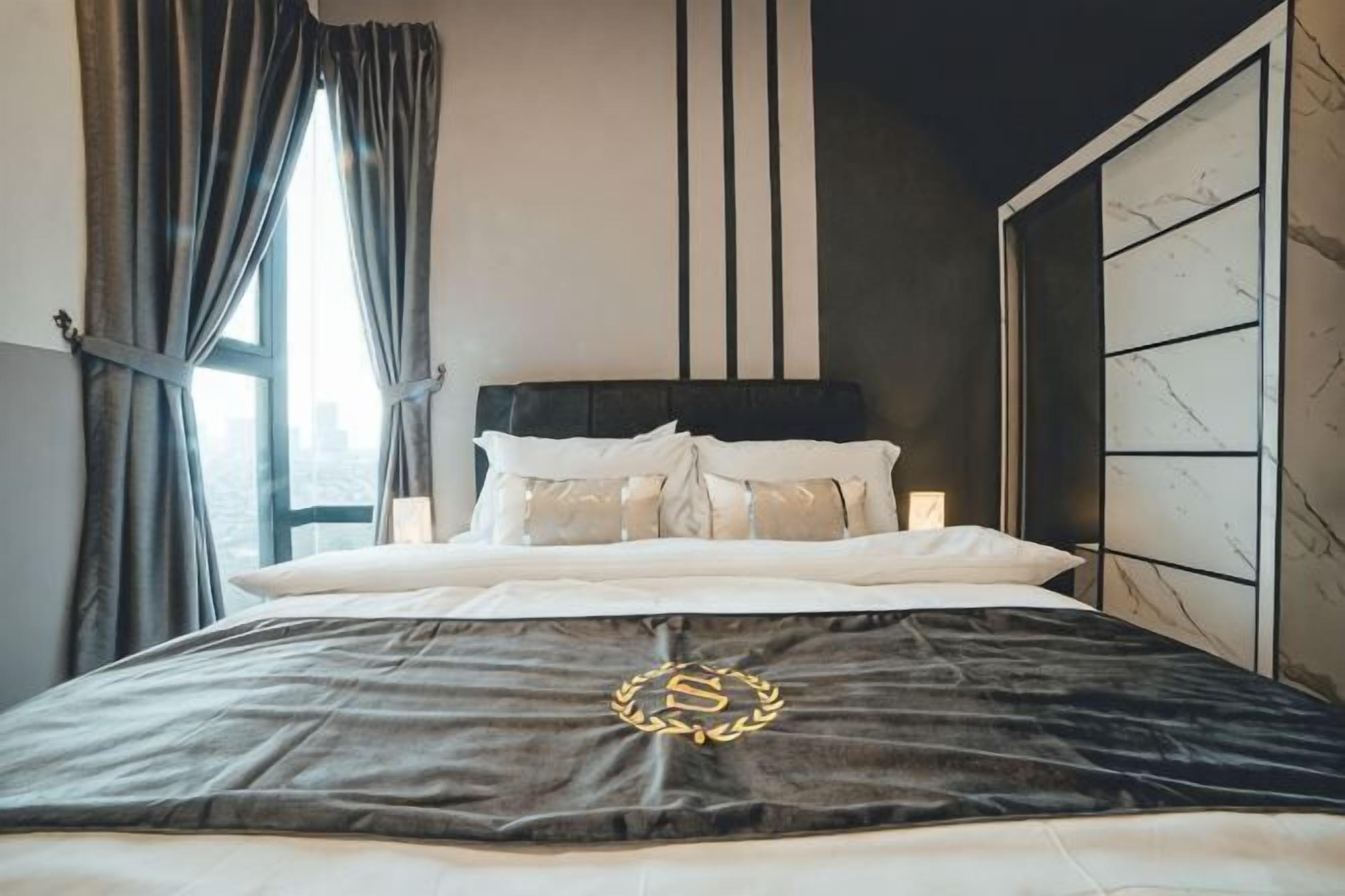 Ein Bett mit dunkler Decke, einem Kopfteil und einem Fenster mit Vorhängen.