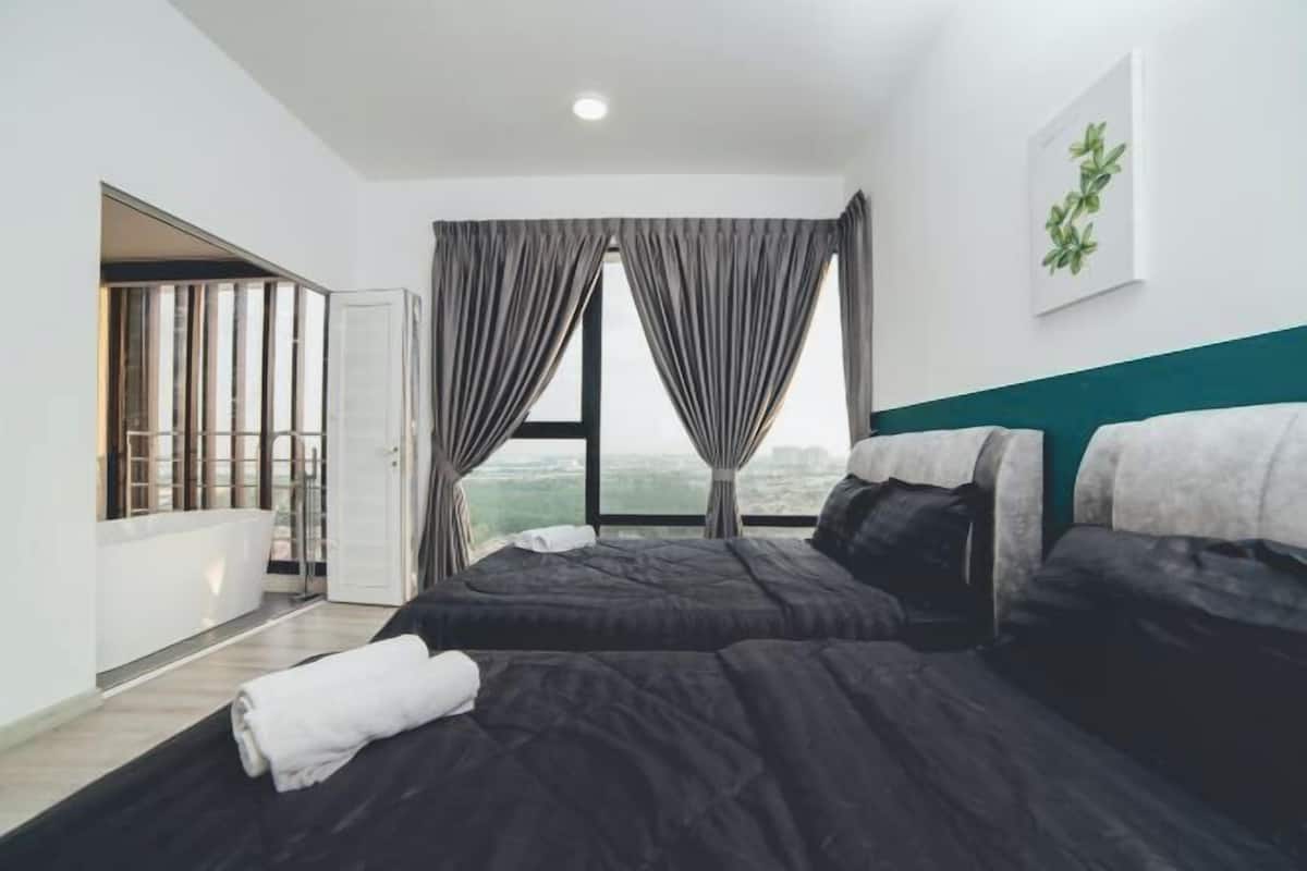 A modern hotel room with two beds, a large window with curtains, a view of the city, and a green accent wall.