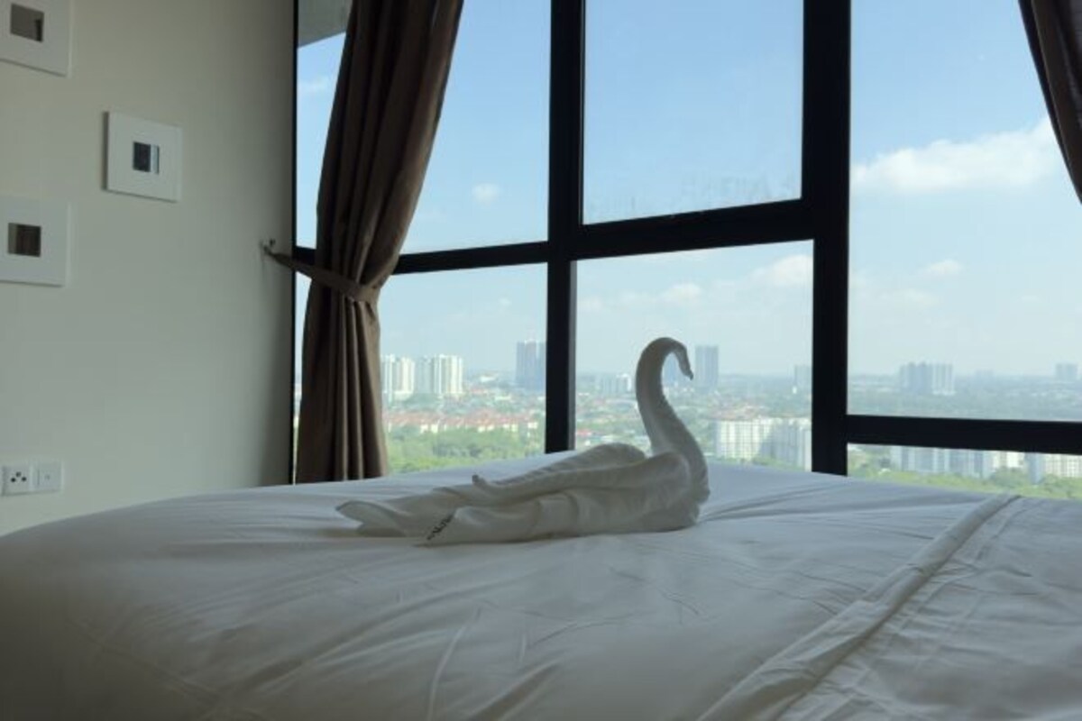 Un lit avec un oreiller en forme de cygne et une vue sur le paysage urbain, visible à travers de grandes fenêtres.