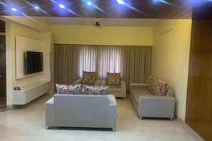 A living room with a sofa set, a flat-screen TV mounted on the wall, and a ceiling fan. - Mahir's Cozy Den (Dhaka)