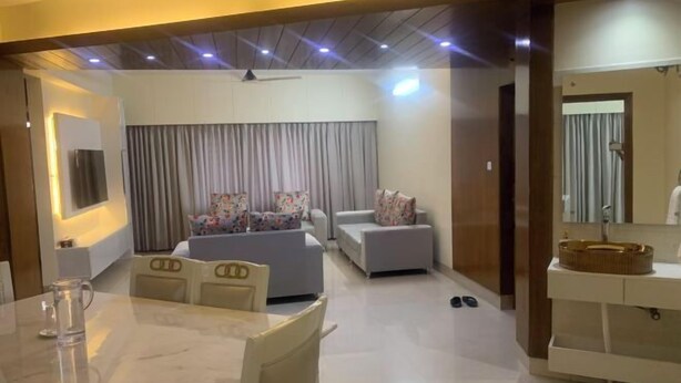 A modern living room with a dining area, a sofa set, a TV mounted on the wall, and a bathroom with a mirror and sink. - Mahir's Cozy Den (Dhaka)