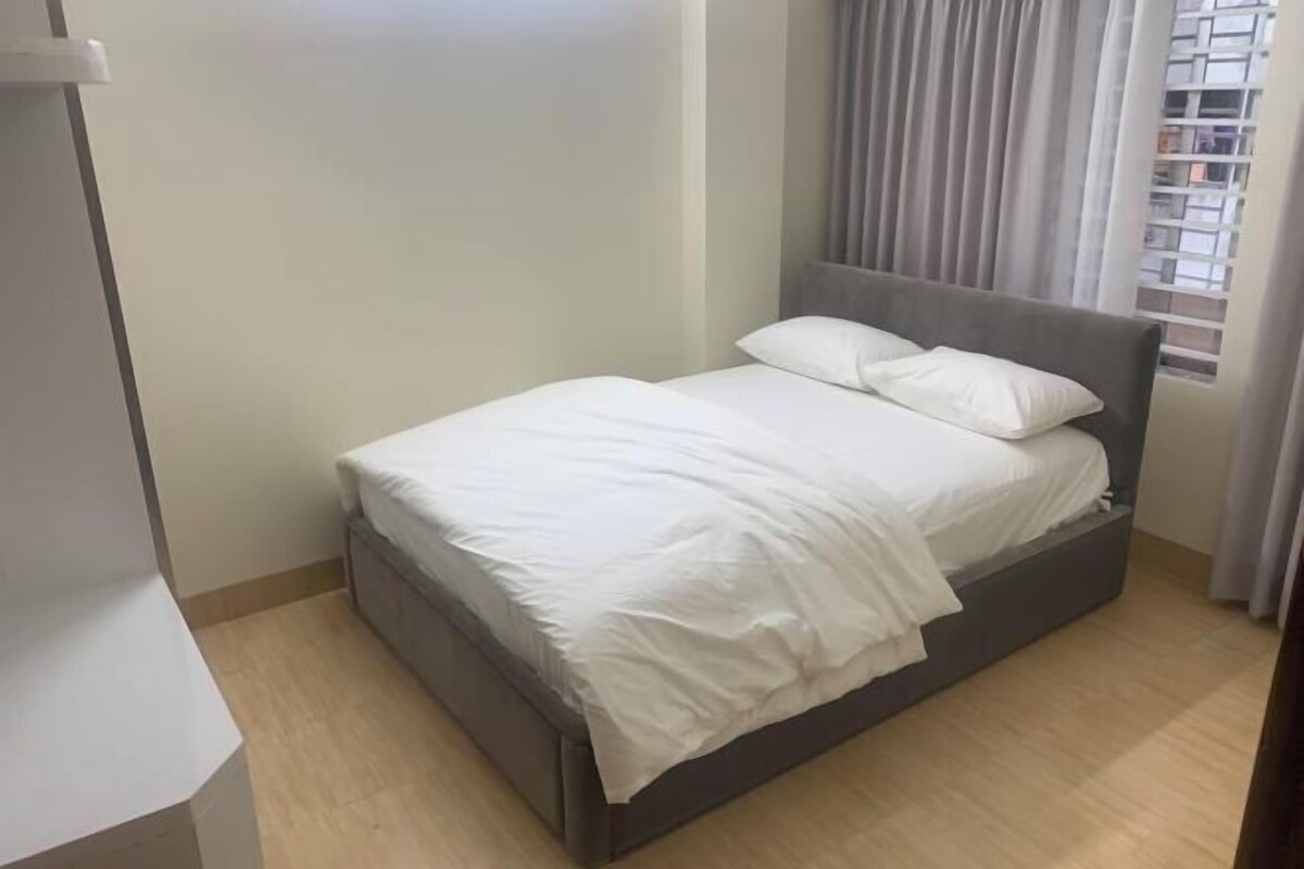 A single bed with white bedding in a room with light-colored walls and a window with curtains.
