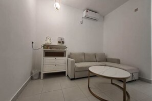 Una habitación con sofá, una mesita, un armario blanco y un equipo de aire acondicionado.