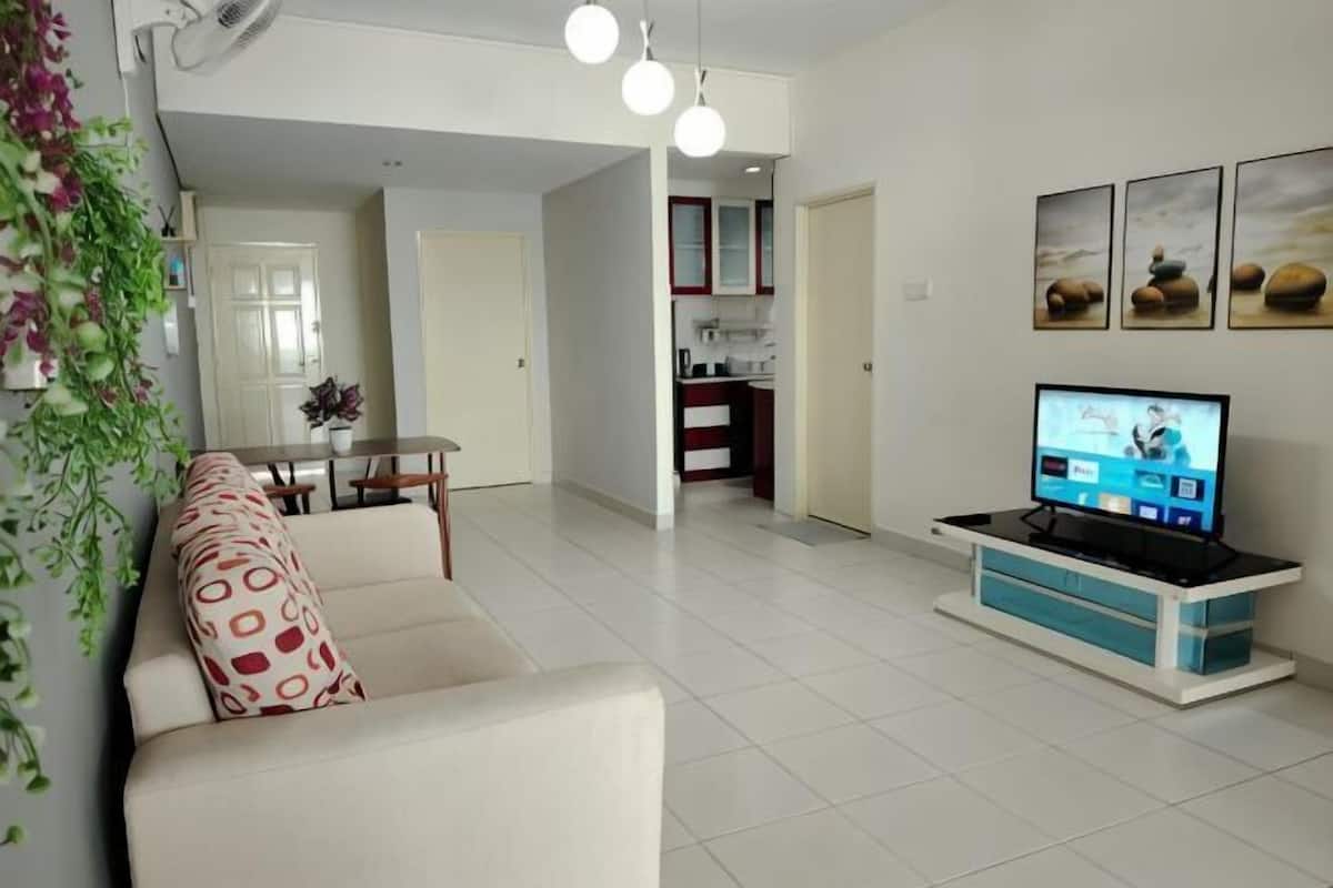 A living room with a sofa, a TV, and a kitchen in the background.