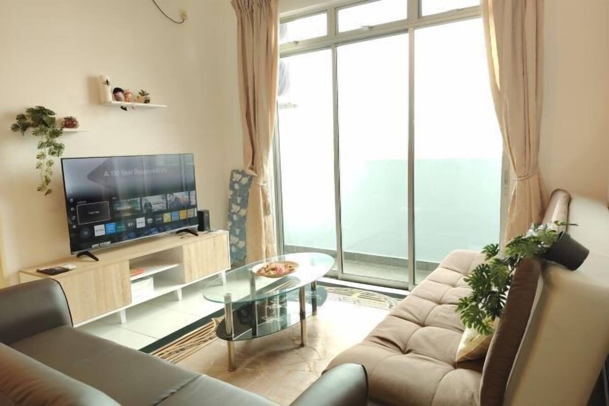 Een woonkamer met een televisie, bank, glazen salontafel en een balkon met gordijnen.