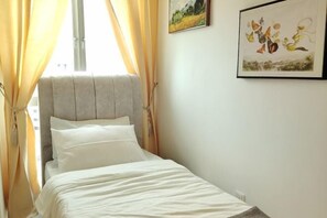 A single bed with a grey headboard, white bedding, and yellow curtains.