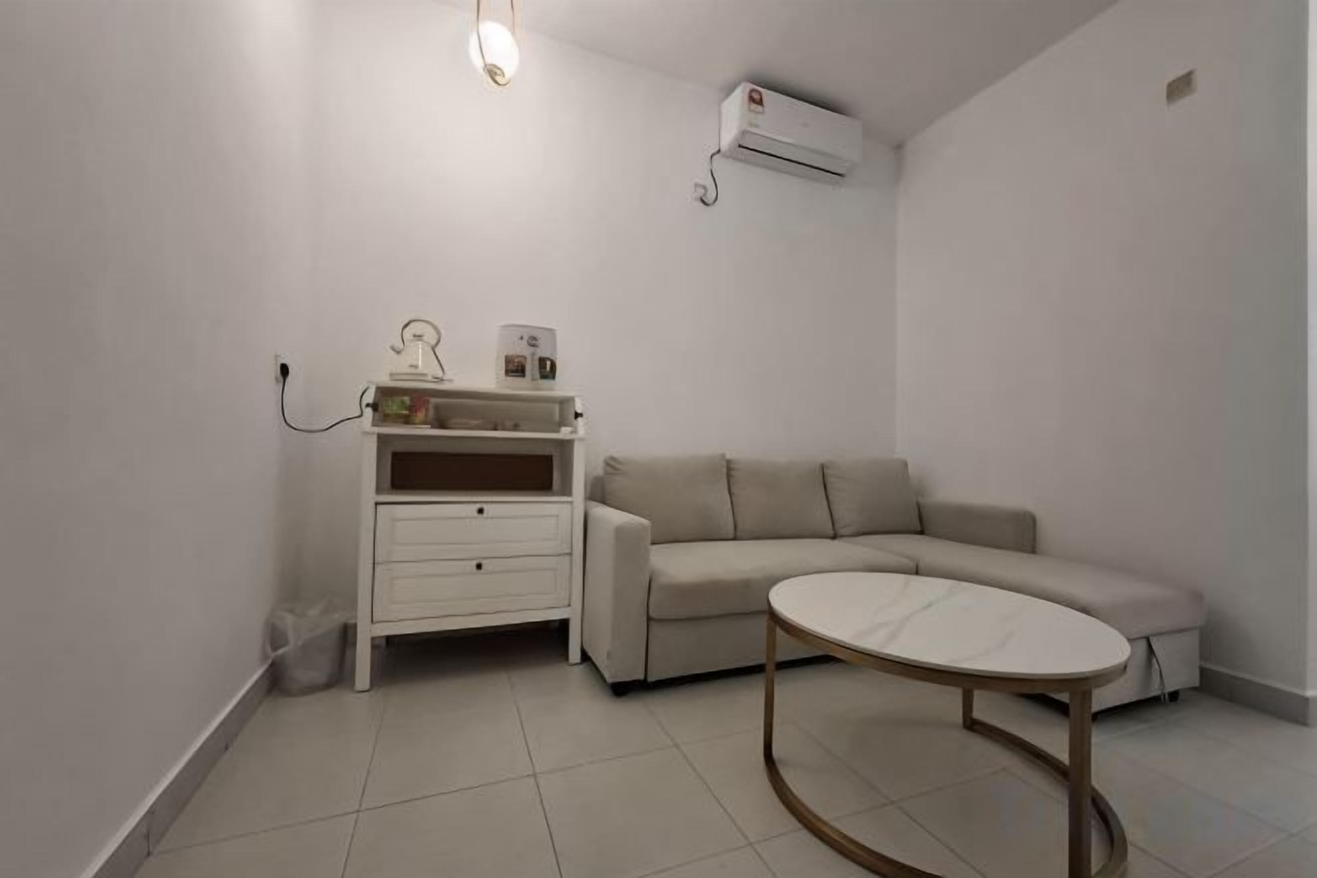 A modern, minimalist living room with a beige sofa, a white side table, and a small white cabinet.