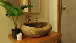 Een badkamer met een houten wastafelmeubel, een stenen wastafel, een plant in pot en een spiegel.