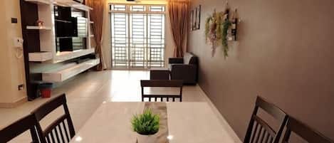 A dining area with a marble table, chairs, a potted plant, a TV, and a sofa in the background.