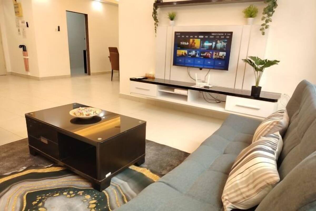 Een moderne woonkamer met een flatscreen televisie, een bank, een salontafel en een kleine plant.