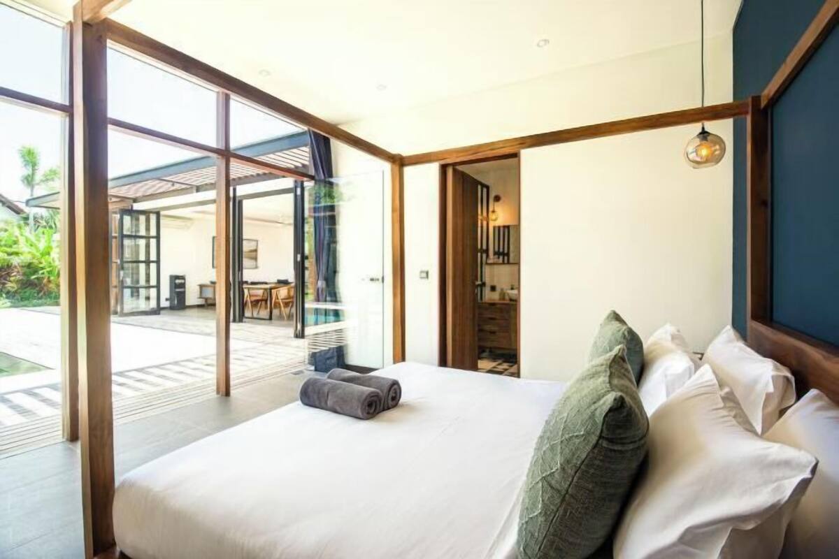 A modern hotel room with a large bed, a view of the outdoor area, and a wooden ceiling structure.