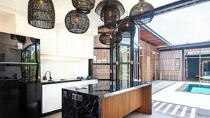 A modern kitchen with a marble island, black pendant lights, and a view of a swimming pool. - Bodhisatva (Bali)