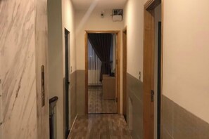 Corredor estreito com uma porta de madeira no final, um interruptor de luz e um aparelho de ar condicionado no teto.