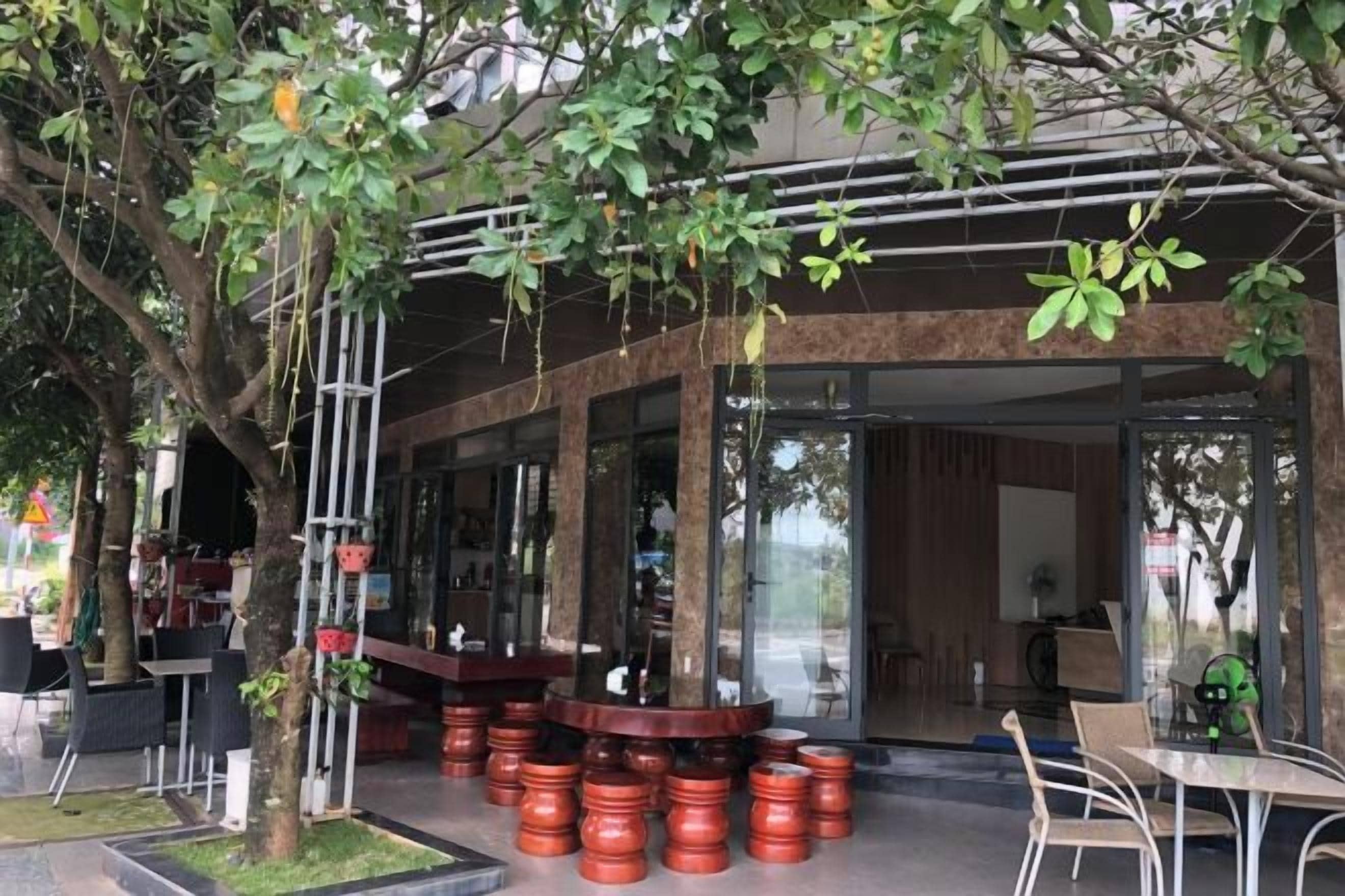 An outdoor seating area with tables and chairs, a tree, and a building entrance.
