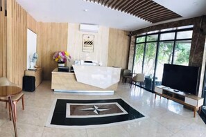 A modern reception area with a reception desk, a flat-screen TV, and a large window offering a view of the outdoors. - Hoang Gia Hotel (Tan Uyen District)