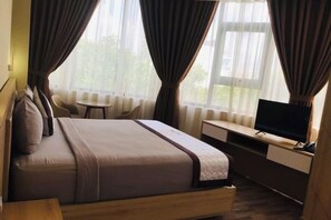 A hotel room with a bed, a desk with a TV, a chair, and a window with curtains. - Hoang Gia Hotel (Tan Uyen District)
