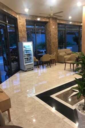 Een ontvangsthal met een marmeren vloer, een plafondventilator, een automaat en een zithoek met stoelen en een bank.