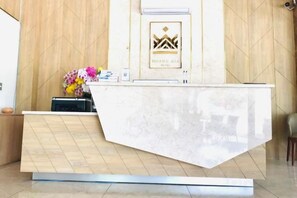 A hotel reception desk with a marble counter, a framed logo above it, and a vase of flowers to the left. - Hoang Gia Hotel (Tan Uyen District)