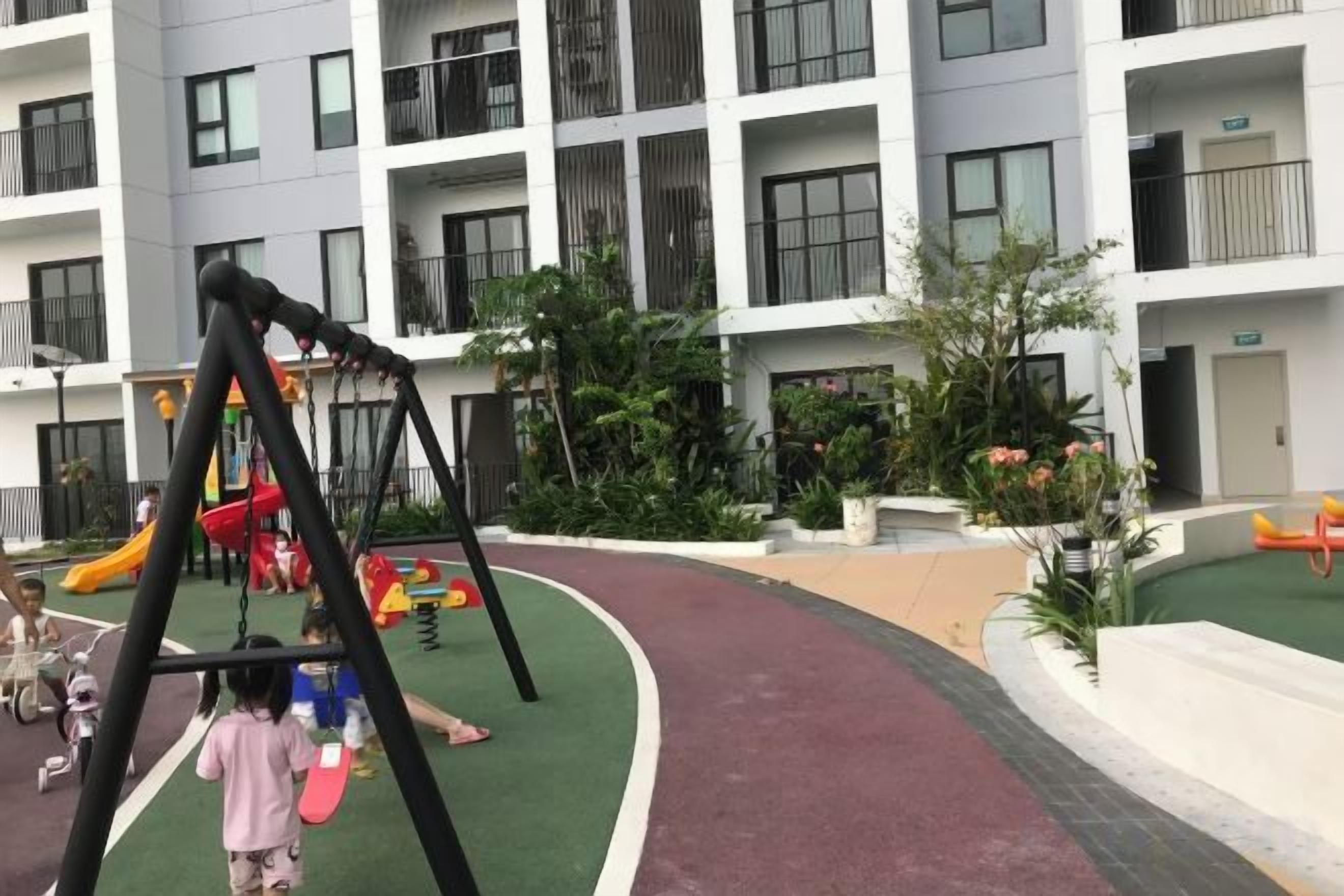 A children's play area with a swing set and a slide, surrounded by a building with balconies and windows.