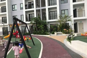 A children's play area with a swing set and a slide, surrounded by a building with balconies and windows. - Hoang Gia Hotel (Tan Uyen District)