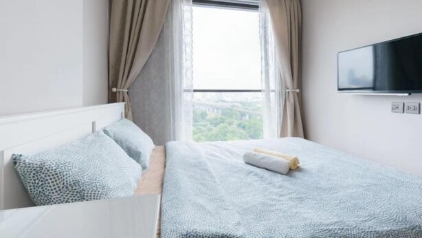A bedroom with a bed, a TV mounted on the wall, and a window with curtains. - Nana Sukhumvit Bangkok Siam Apartment (Bangkok)