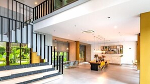 A spacious, modern interior with a staircase leading to an upper level, a dining area with a kitchen in the background, and a view of greenery outside. - Nana Sukhumvit Bangkok Siam Apartment (Bangkok)