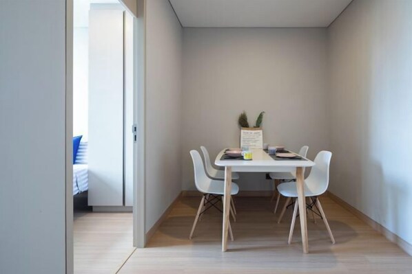 A small, modern dining area with a table and four chairs, a small plant on the table, and a door leading to another room. - Nana Sukhumvit Bangkok Siam Apartment (Bangkok)