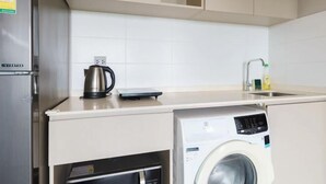 A compact kitchen with a built-in washing machine, a kettle, and a sink. - Nana Sukhumvit Bangkok Siam Apartment (Bangkok)