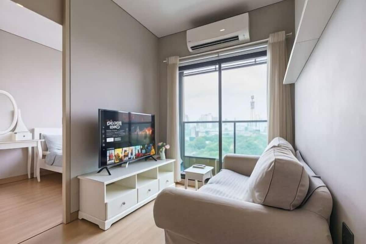 Ein modernes Wohnzimmer mit Flachbildfernseher, einer Couch, einem kleinen Tisch und einem großen Fenster mit Blick auf die Stadt.
