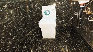 A bathroom with a black marble floor and walls, a white toilet, and a shower area with a white sink and faucet. - Hotel Royal Krishna (Gorakhpur)